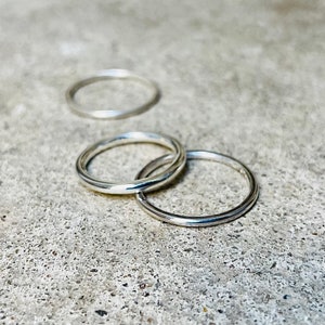 Puede incluir: Tres anillos de plata de diferentes tamaños, apilados uno encima del otro, sobre una superficie gris texturizada.