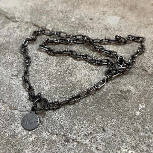 Könnte beinhalten: Eine silberne Kettenkette mit einem Schiebeverschluss und einem runden Anhänger, auf dem "925" steht.