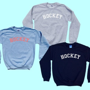 Pu&ograve; includere: Tre felpe con la parola "HOCKEY" stampata sul davanti. Una felpa &egrave; azzurra con la parola in rosa, una &egrave; grigia con la parola in bianco e l'ultima &egrave; blu scuro con la parola in bianco.