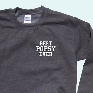 May include: A dark gray sweatshirt with the text "BEST POPSY EVER" printed in white on the front.