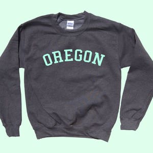 May include: A dark gray sweatshirt with the word "OREGON" printed in light green on the front.