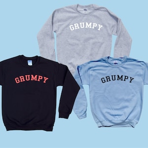 May include: Three long-sleeved sweatshirts with the word "GRUMPY" printed on the front in different colors. The sweatshirts are in black, light blue, and gray.
