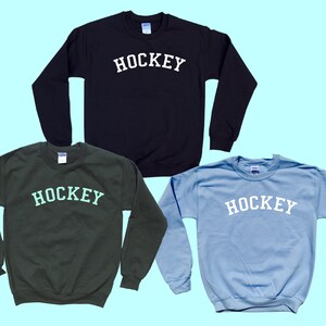 Pu&ograve; includere: Tre felpe in nero, verde e azzurro chiaro con la scritta "HOCKEY" stampata in bianco sul davanti.