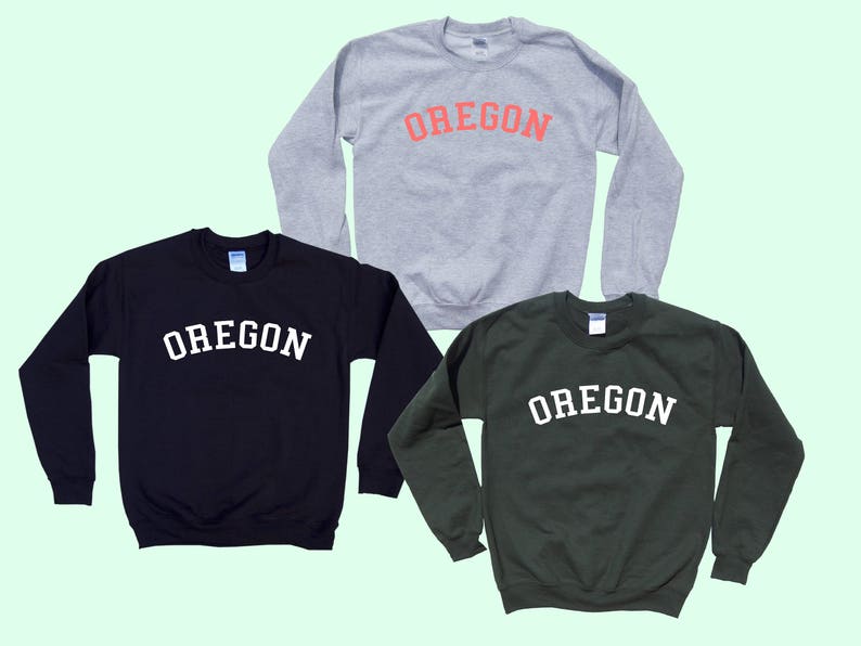 May include: Three sweatshirts in different colors, gray, black, and green, with the word "OREGON" printed in white on each. The word "OREGON" is in an arched font.