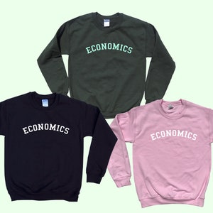 May include: Three sweatshirts with the word "ECONOMICS" printed on the front in an arched font. The sweatshirts are in black, green, and pink.