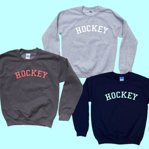 Pu&ograve; includere: Tre felpe con la scritta "HOCKEY" stampata sul davanti. Le felpe sono di colore grigio, grigio scuro e blu navy. La scritta "HOCKEY" &egrave; in bianco sulla felpa grigia, in rosso sulla felpa grigio scuro e in azzurro sulla felpa blu navy.