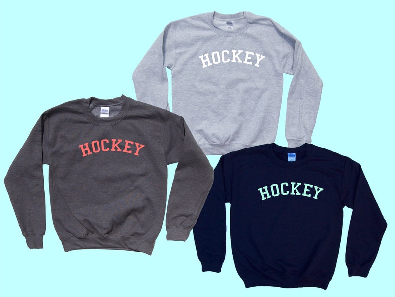 Pu&ograve; includere: Tre felpe con la scritta "HOCKEY" stampata sul davanti. Le felpe sono di colore grigio, grigio scuro e blu navy. La scritta "HOCKEY" &egrave; in bianco sulla felpa grigia, in rosso sulla felpa grigio scuro e in azzurro sulla felpa blu navy.