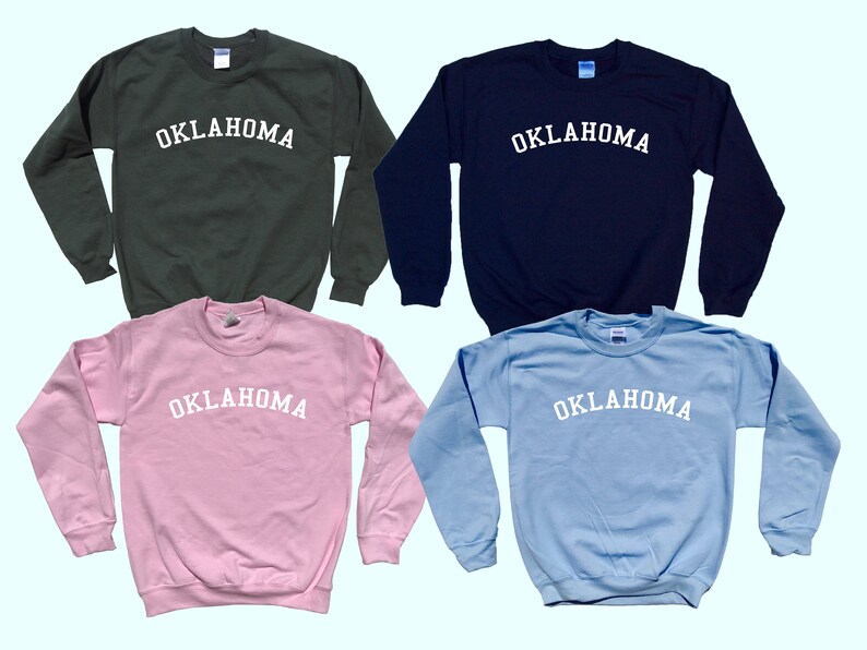 May include: Four sweatshirts in different colors: dark green, navy blue, light pink, and light blue. Each sweatshirt has the word "OKLAHOMA" printed in white on the front.