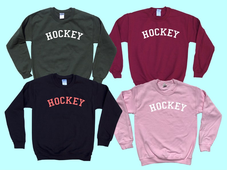 Pu&ograve; includere: Quattro felpe di diversi colori con la parola "HOCKEY" stampata in un arco bianco sul davanti. Le felpe sono di colore verde, bordeaux, nero e rosa.