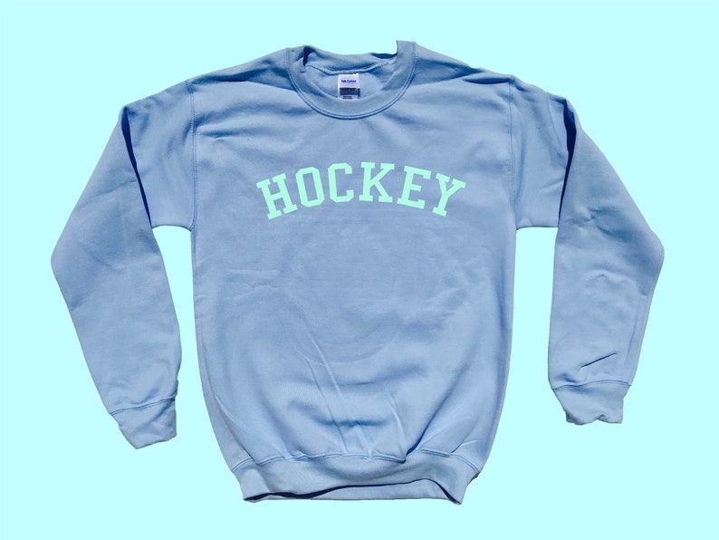 Pu&ograve; includere: Una felpa blu chiaro con la parola "HOCKEY" stampata in verde chiaro sul petto.