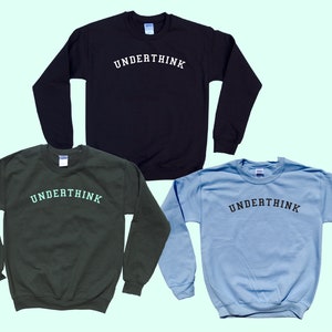 May include: Three crew neck sweatshirts in black, dark green, and light blue. Each sweatshirt features the word "UNDERTHINK" arched across the chest in a contrasting colour. The sweatshirts are displayed on a light green background.