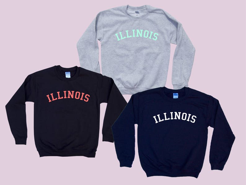 May include: Three sweatshirts in different colors with the word "ILLINOIS" printed in a varsity-style font. The sweatshirts are gray, black, and navy blue.