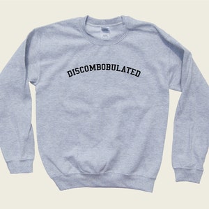 May include: A light gray sweatshirt with the word "DISCOMBOBULATED" arched across the chest in black, block letters. The sweatshirt has a crew neck and long sleeves.