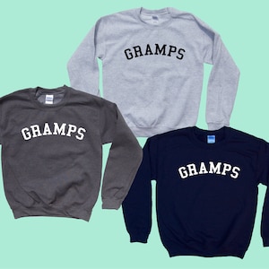 May include: Three sweatshirts with the word "GRAMPS" printed in a white arch across the front. The sweatshirts are in gray, dark gray, and navy blue.