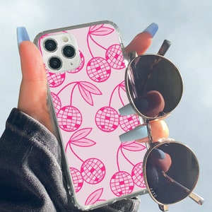 May include: A pink phone case with a pattern of pink cherries with a disco ball design. The case is clear and shows the phone's camera lens.