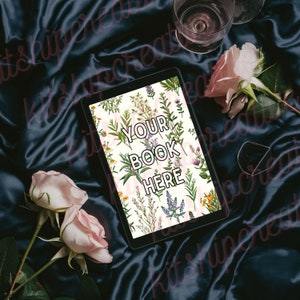 K&ouml;nnte beinhalten: Ein Tablet-Computer mit einem floralen Design und dem Text "YOUR BOOK HERE" auf dem Bildschirm. Das Tablet liegt auf einem dunkelblauen Satin-Stoff mit rosa Rosen.