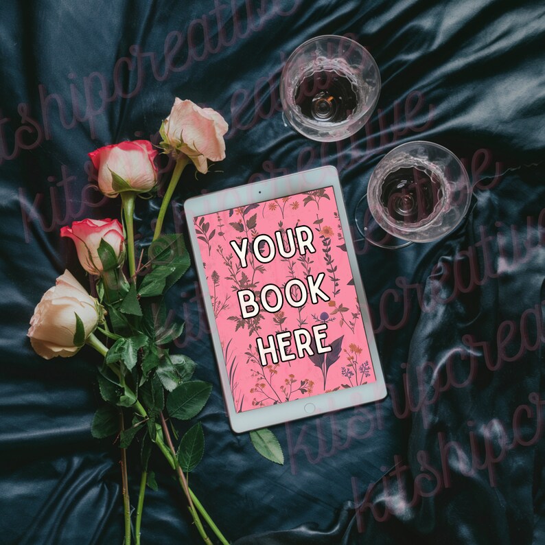 K&ouml;nnte beinhalten: Ein wei&szlig;es Tablet mit einem rosafarbenen Blumenhintergrund und dem Text "YOUR BOOK HERE" auf dem Bildschirm. Das Tablet liegt auf einer dunkelblauen Stoffoberfl&auml;che mit rosa Rosen und zwei klaren Glasbechern.