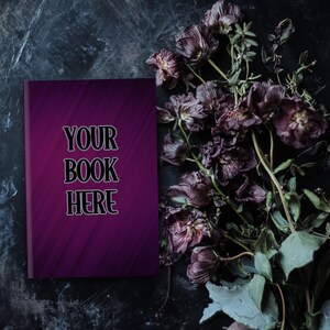 Może przedstawiać: Makieta okładki książki w ciemnym fioletowym kolorze z tekstem "YOUR BOOK HERE" na ciemnym tle z suszonymi fioletowymi kwiatami.