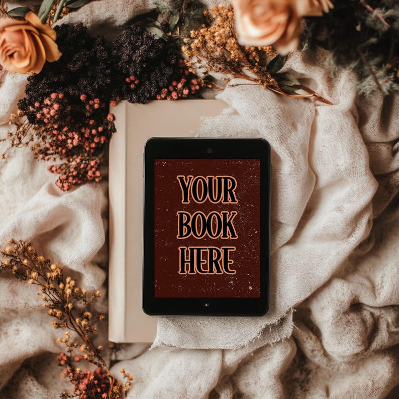 Może przedstawiać: Czarny tablet z białą okładką książki na białym tle z tkaniny. Ekran tabletu wyświetla tekst "YOUR BOOK HERE" w kolorze pomarańczowym na czerwonym tle.