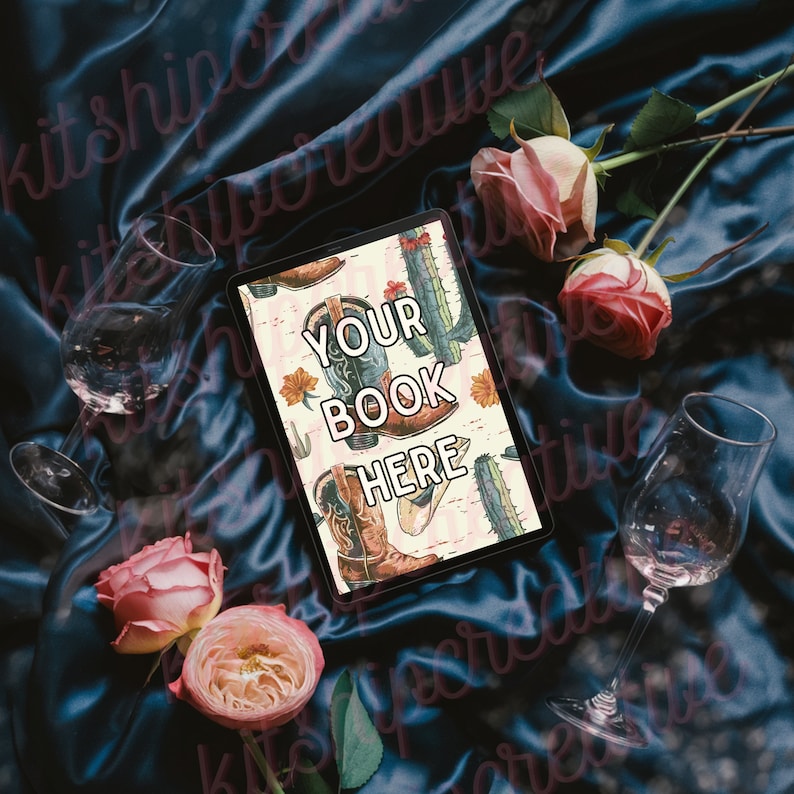 K&ouml;nnte beinhalten: Ein digitales Tablet mit einem rosa und wei&szlig;en Hintergrund, der ein Muster aus Cowboystiefeln und Kakteen zeigt. Der Text "YOUR BOOK HERE" wird auf dem Bildschirm angezeigt. Das Tablet liegt auf einem blauen Satin-Stoff mit rosa Rosen und Weingl&auml;sern.