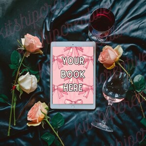 K&ouml;nnte beinhalten: Ein wei&szlig;es Tablet mit rosa Hintergrund und dem Text "YOUR BOOK HERE" auf dem Bildschirm. Das Tablet ist von rosa Rosen und zwei Gl&auml;sern Wein auf einer dunkelblauen Oberfl&auml;che umgeben.