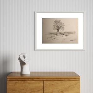 Peut inclure: Dessin en noir et blanc encadré d'un grand arbre dans un champ. L'œuvre est dans un cadre blanc et est suspendue au-dessus d'une commode en bois. Une sculpture de tête en céramique blanche est sur la commode.