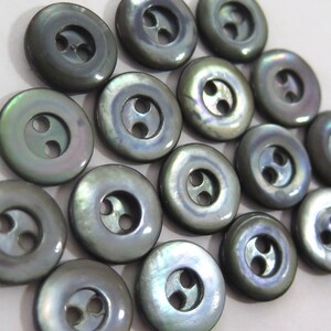 May include: A group of 17 iridescent black shell buttons with two holes each. The buttons are round and have a smooth, polished finish.
