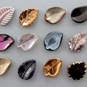May include: Assortment of 15 leaf-shaped glass buttons in various colours and finishes, including iridescent, metallic, and clear.