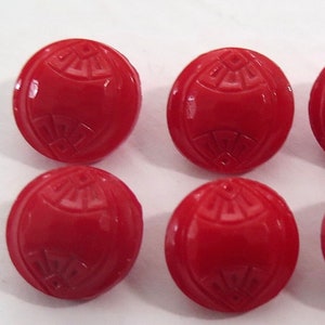Könnte beinhalten: Sechs rote Plastikknöpfe mit einem dekorativen Design. Die Knöpfe sind rund und haben ein erhabenes Design.