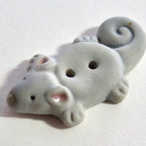 Può includere: Bottone in ceramica grigio chiaro a forma di topo. Il topo ha una coda arricciata, due fori per cucire e dettagli rosa sulle orecchie e sul naso. Fornitura artigianale.