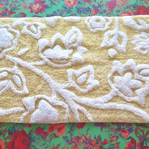 May include: A rectangular bath mat with a yellow background and a white floral design. The mat has a textured, raised pattern. The mat is approximately 30 inches long and 20 inches wide.