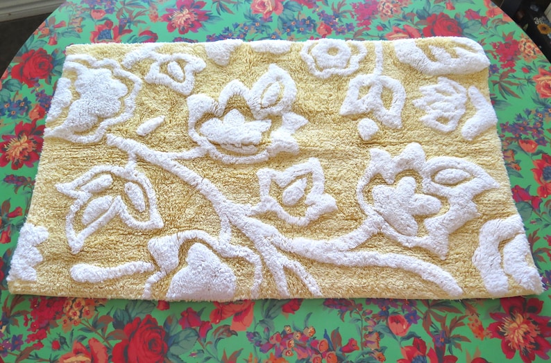 May include: A rectangular bath mat with a yellow background and a white floral design. The mat has a textured, raised pattern. The mat is approximately 30 inches long and 20 inches wide.