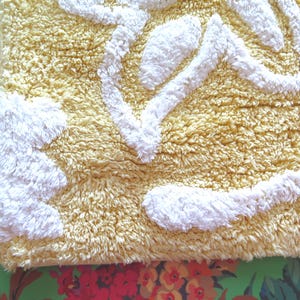 May include: A rectangular, textured bath mat with a yellow background and white, raised abstract shapes. The mat has a soft, plush appearance, suggesting a comfortable and absorbent design for bathroom use.