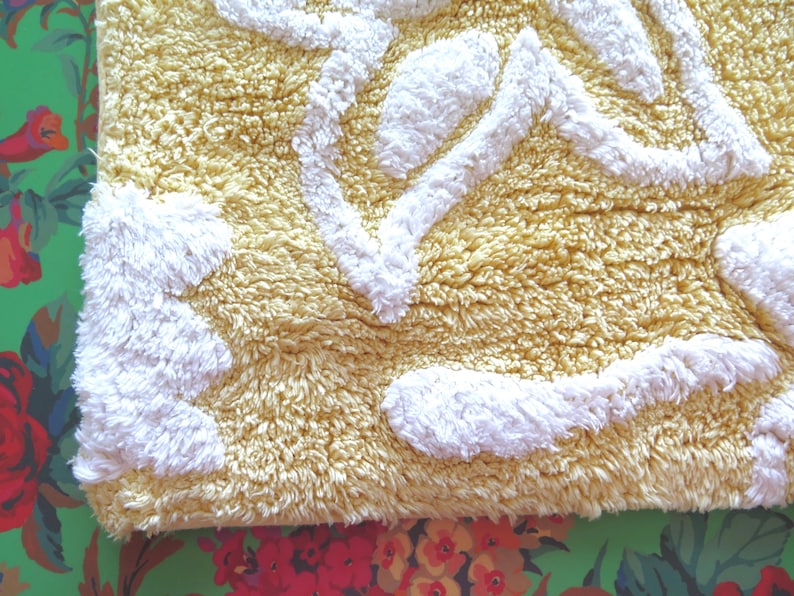 May include: A rectangular, textured bath mat with a yellow background and white, raised abstract shapes. The mat has a soft, plush appearance, suggesting a comfortable and absorbent design for bathroom use.