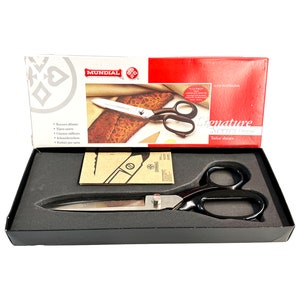 May include: A black and silver pair of Mundial Signature Series tailor shears in a black box with a red and white box lid. The lid features the Mundial logo and the text "Signature Series Tailor Shears".