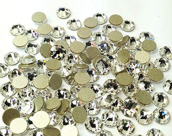 May include: A large quantity of clear glass rhinestones with silver backing. The rhinestones are scattered on a white surface.