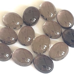 Peut inclure: Une collection de 12 pierres précieuses de quartz fumé de forme ovale. Les pierres sont de couleur brun foncé et ont une finition lisse et polie.