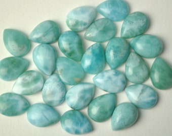 May include: A collection of 25 teardrop-shaped, light blue and white, seafoam cabochons. The cabochons are smooth and polished.