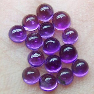 Puede incluir: Un conjunto de piedras preciosas redondas y translúcidas de amatista púrpura. Las piedras pulidas tienen un acabado brillante, que refleja la luz. Las piedras preciosas varían ligeramente de tamaño y están dispuestas juntas, mostrando su color y claridad naturales.