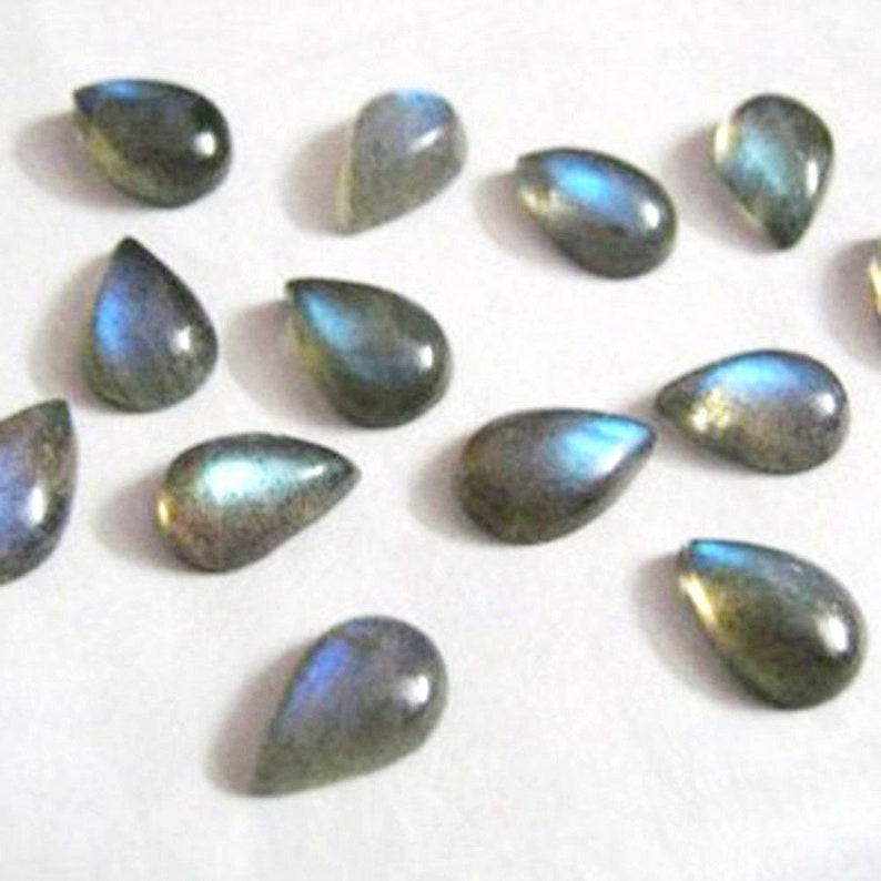 May include: A collection of 12 teardrop-shaped labradorite gemstone cabochons. The stones are a dark grey colour with iridescent blue and green flashes.
