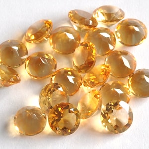 Op de afbeelding: Een verzameling van 20 gefacetteerde, ronde topaas edelstenen. De edelstenen zijn licht tot middelmatig amberkleurig en hebben een hoge glans.