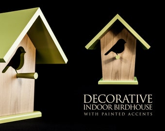 May include: A decorative indoor birdhouse with a green roof and a silhouette of a bird on the front. The birdhouse is made of wood and has a perch for the bird to sit on. The text "DECORATIVE INDOOR BIRDHOUSE WITH PAINTED ACCENTS" is printed below the birdhouse.