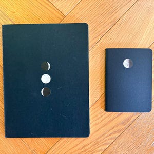以下が含まれることがあります： 月の満ち欠けが印刷された黒いノートが2冊。大きいノートには月の満ち欠けが3つ、小さいノートには1つ印刷されています。