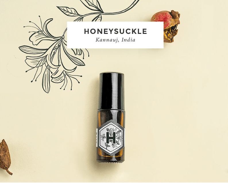 May include: A small brown glass bottle with a black rollerball top. The bottle has a white label with a black hexagonal design and the letter "H" inside. The label also says "Honeysuckle Kannauj, India".