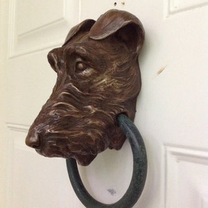 May include: A bronze door knocker shaped like a dog's head with a green metal ring.