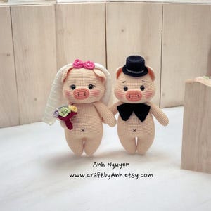 May include: Two crocheted pig plushies dressed as a bride and groom. The bride pig is wearing a white veil and holding a bouquet of flowers. The groom pig is wearing a black top hat and bow tie. The pigs are standing on a wooden surface.