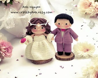 May include: Crocheted wedding couple figurines. The bride is wearing a white dress with a flower crown and holding a pink flower. The groom is wearing a purple suit with a bow tie. They are standing on wooden bases.