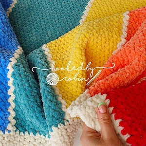 May include: A rainbow crochet blanket with a white border. The blanket is made with a soft, fluffy yarn and is perfect for cuddling up on the couch.