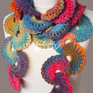 May include: A colourful crocheted scarf with a repeating pattern of circles. The scarf is made with a variety of shades of blue, pink, orange, and yellow yarn.