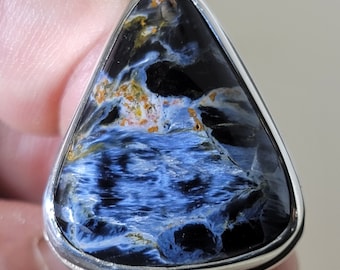 May include: A triangular silver ring with a blue and black tiger's eye gemstone. The gemstone has a swirling pattern of blue and black with hints of gold.